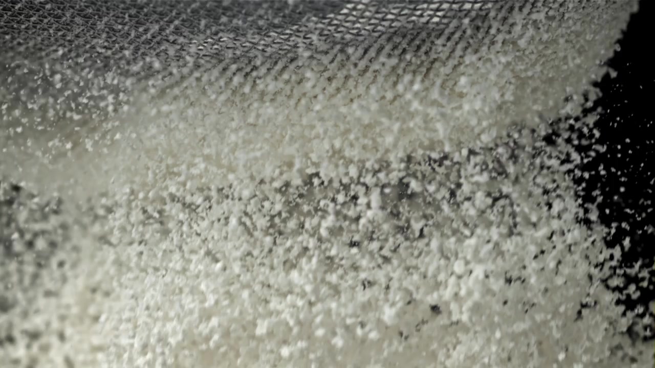 Sigtning af hvide granulat gennem en finmasket si i slowmotion