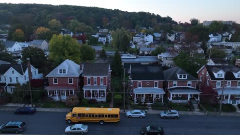 yellow school bus driving past townhouses at dawn