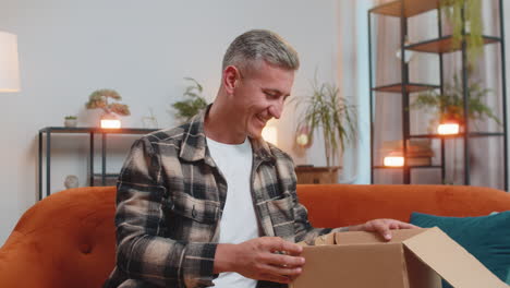 happy customer man unpacking delivery parcel opening cardboard box receiving purchase gift at home