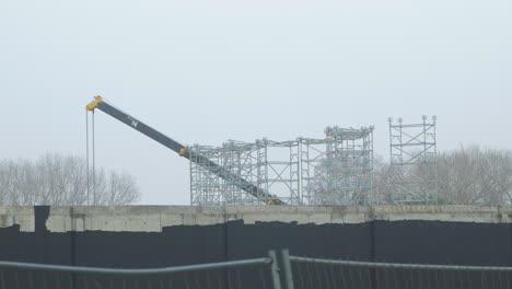 intensive work on the construction site located near the coast of the sea, mobile crane moving, overcast day with fog, distant wide shot