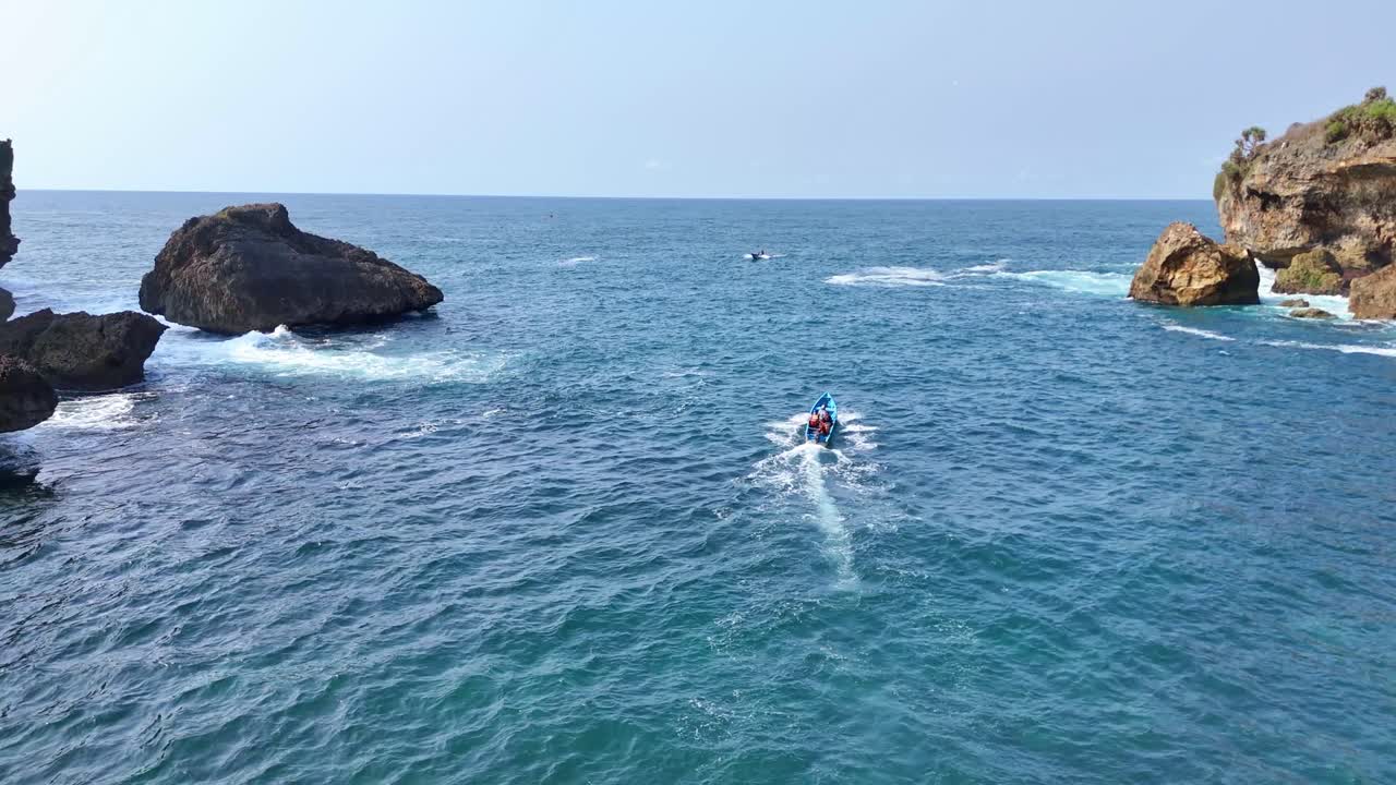 Drone shot following the fisherman boat running to the ocean. The sea water is blue with a horizon that blends with the blue sky. Aerial view of nautical tropical beach. Ngrenehan Beach, Indonesia.