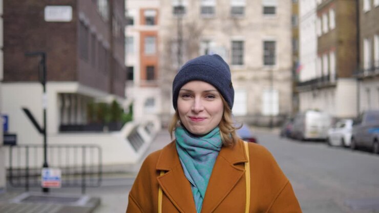 Giovane donna caucasica felice, allegra e positiva che cammina per una strada di Londra, guardando la telecamera e sorridendo