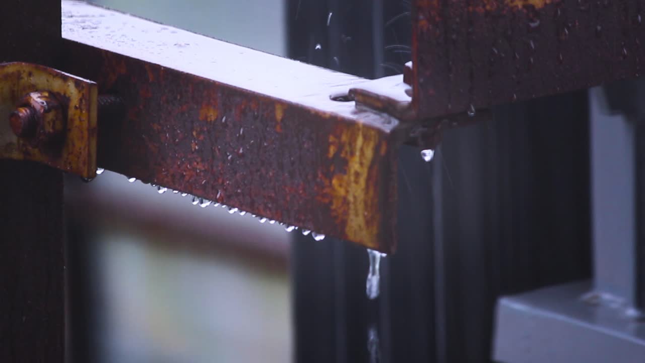 Close-up view of rusty iron beam dripping water during rainfall. Calm rainy weather, perfect for mood, nature or urban decay themes