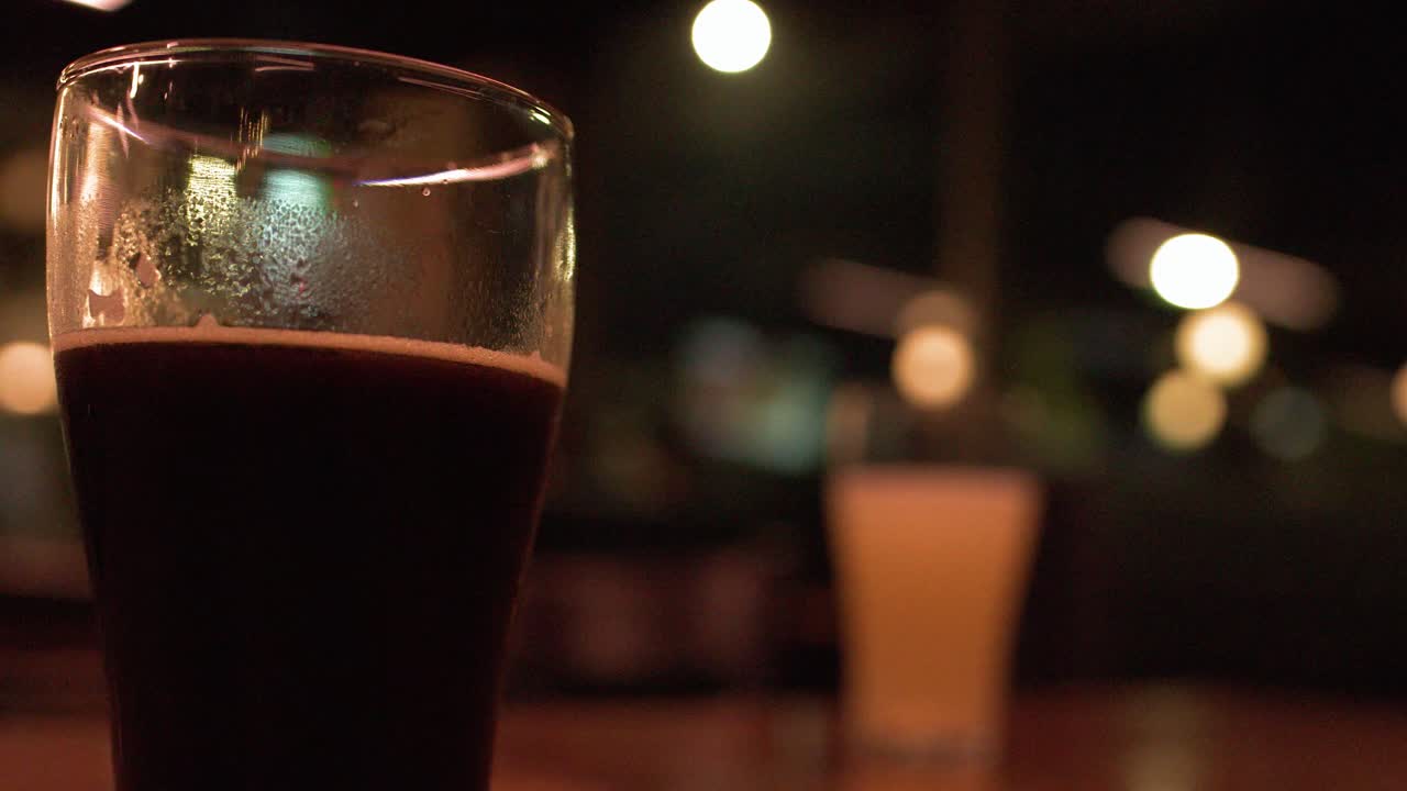 Una pinta di birra scura stout è appoggiata su un tavolo di legno in un bar poco illuminato