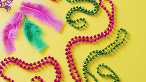 video of pink mask, mardi gras carnival beads and feathers on yellow background with copy space