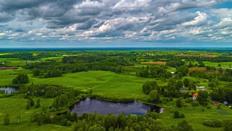 stunning aerial time-lapse showcasing picturesque latvian farmlands with serene lakes, scattered forests, lush green meadows, and charming small cottage houses under a sky of moving clouds