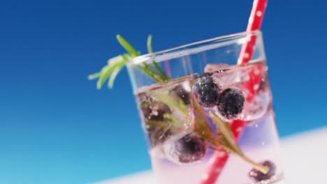 Close-up-of-transparent-drink-with-bluberries-on-blue-background