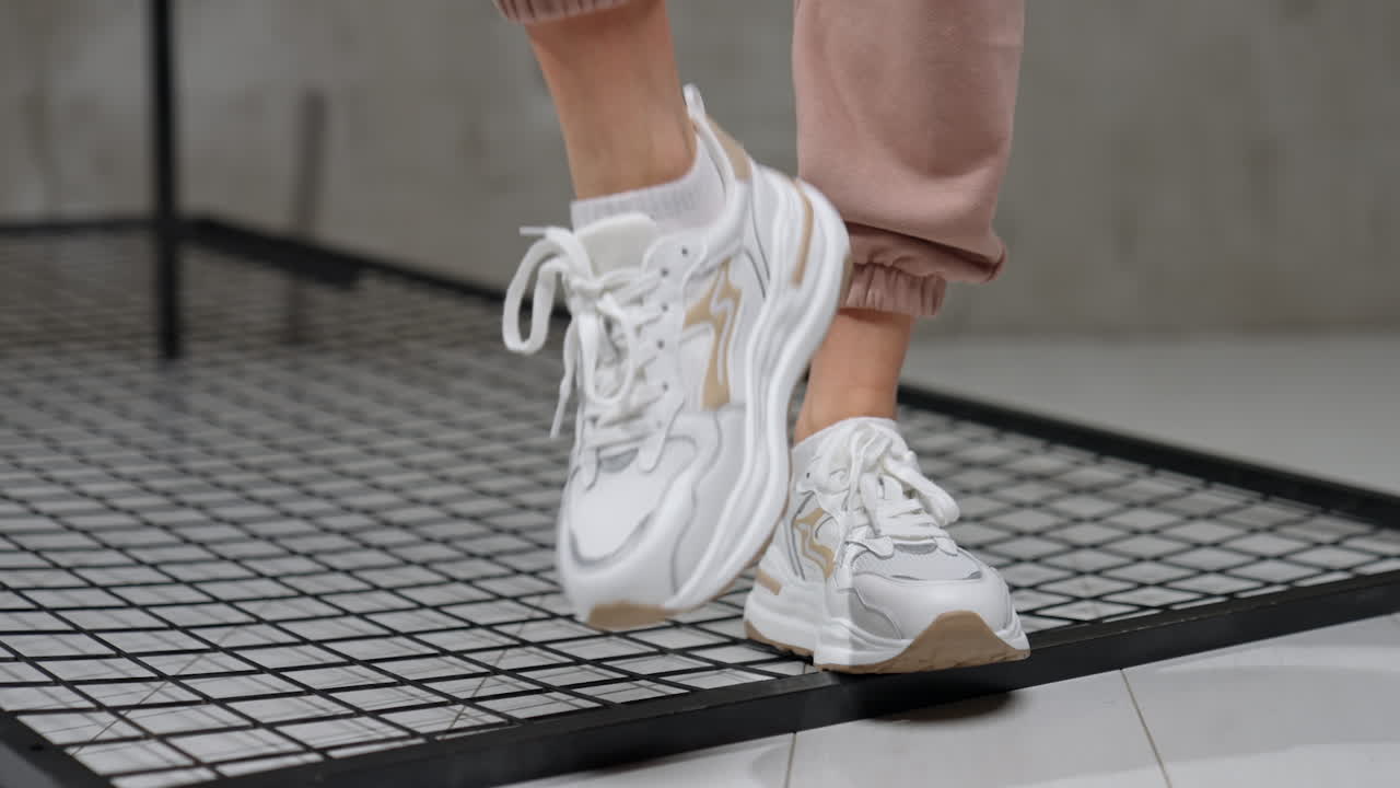 Trendy white sneakers with beige gussets. Model walks by the metal grate in the studio. Close up.