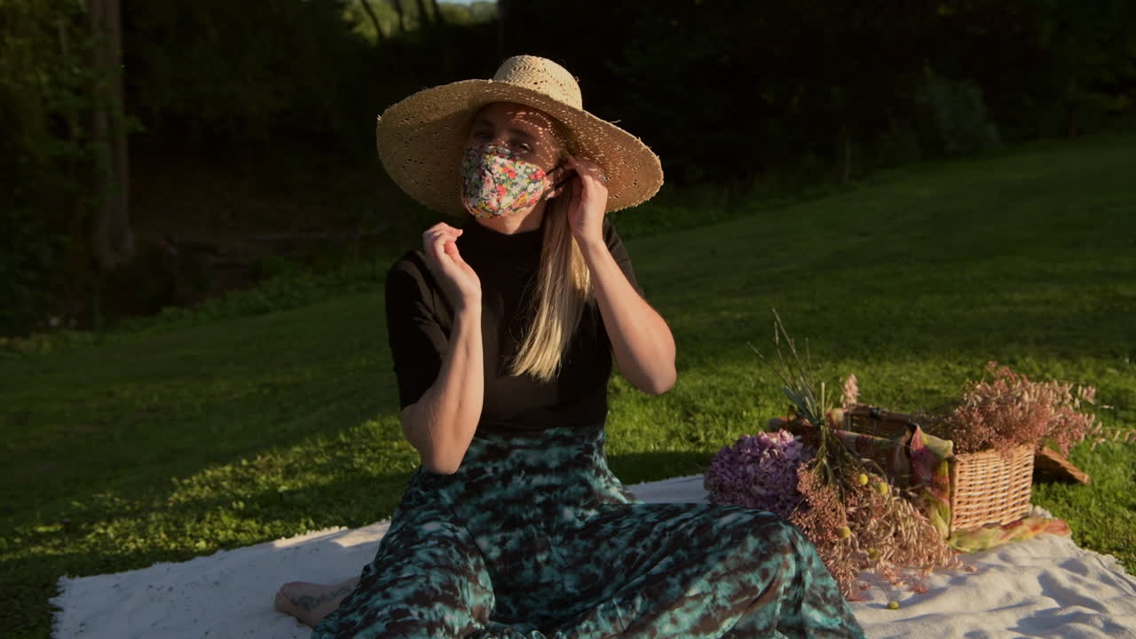 Fashionable girl with hat applying face mask for coronavirus pandemic prevention at the park
