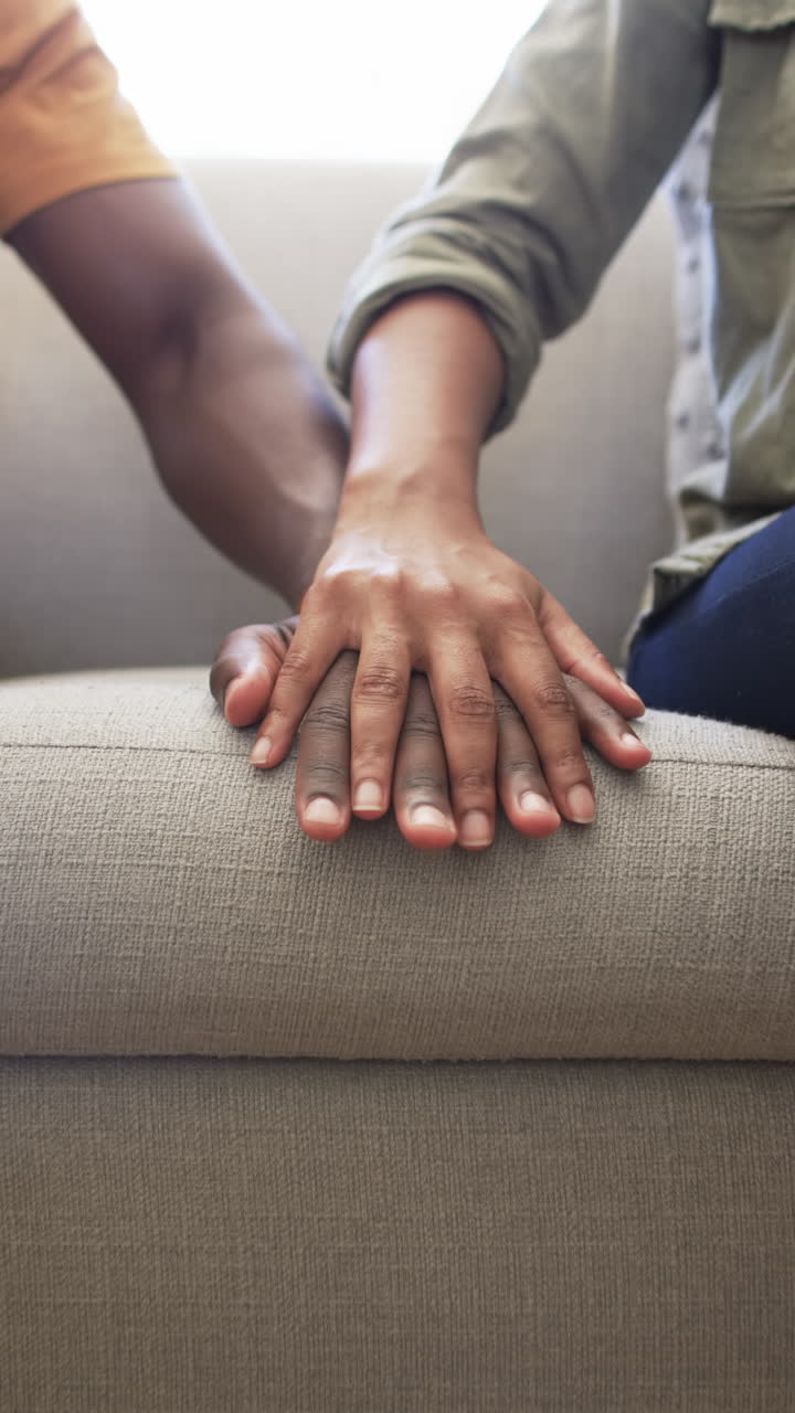 Vertical video: Couple holding hands on couch, showing affection and support at home