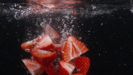 a cámara lenta en rodajas frescas fresas hermosas caen en el agua con burbujas