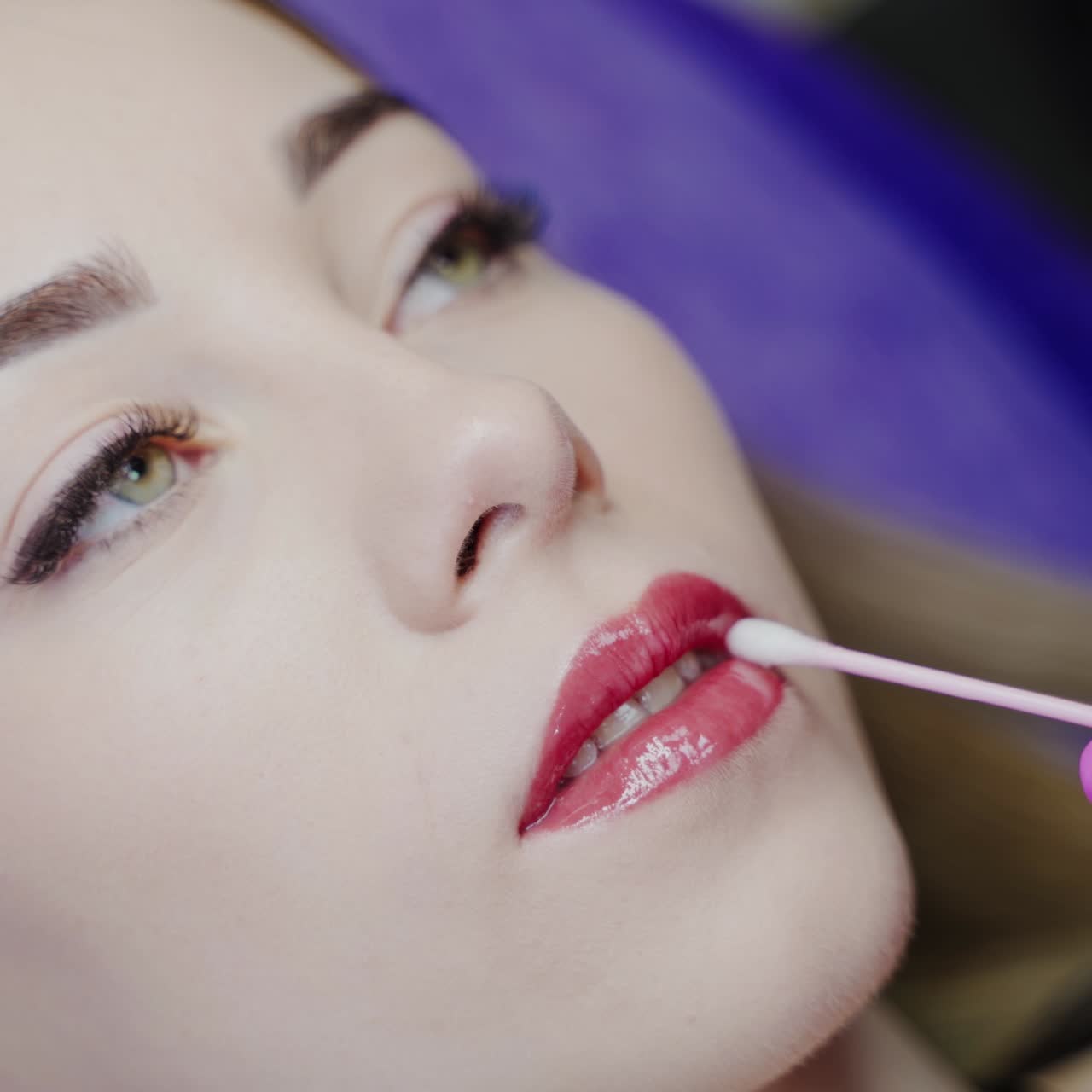 Permanent lips make-up. Cosmetologist finishes the cosmetic procedure on lips to a lovely female client. Close-up.