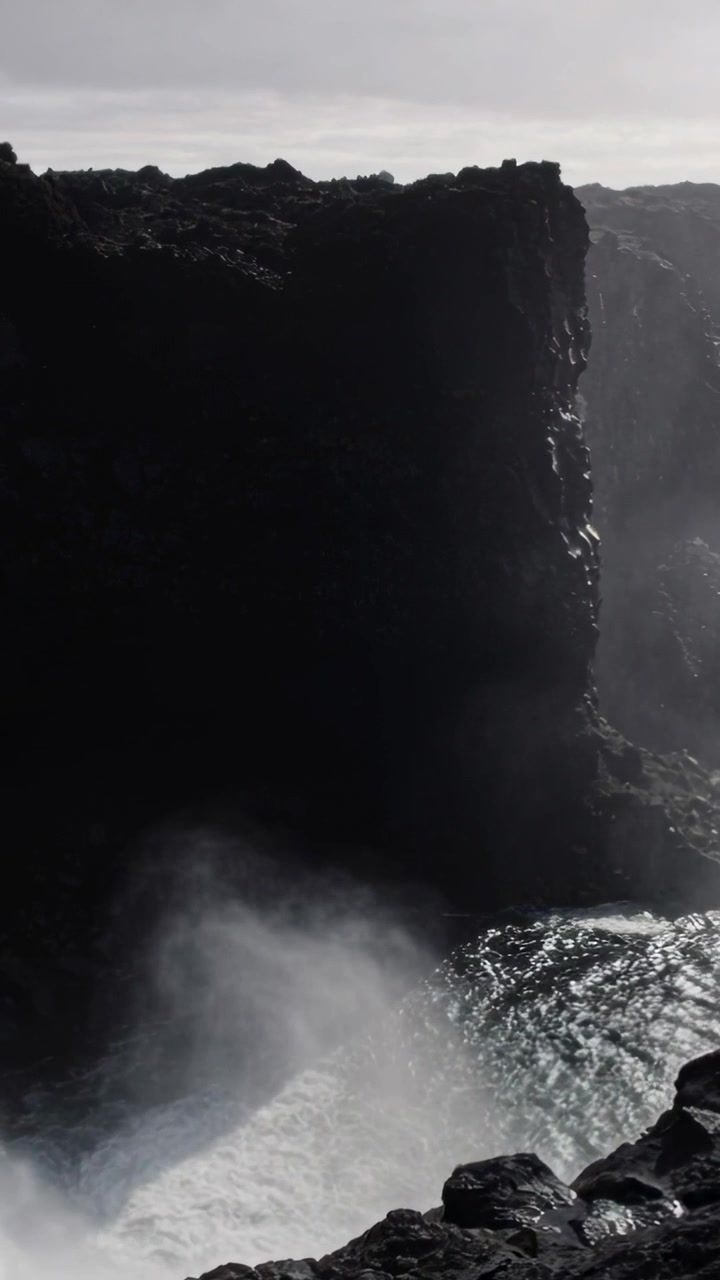 Video vertical: Fuerte oleaje oceánico golpeando un alto acantilado costero, espuma impulsada por el viento rociando.