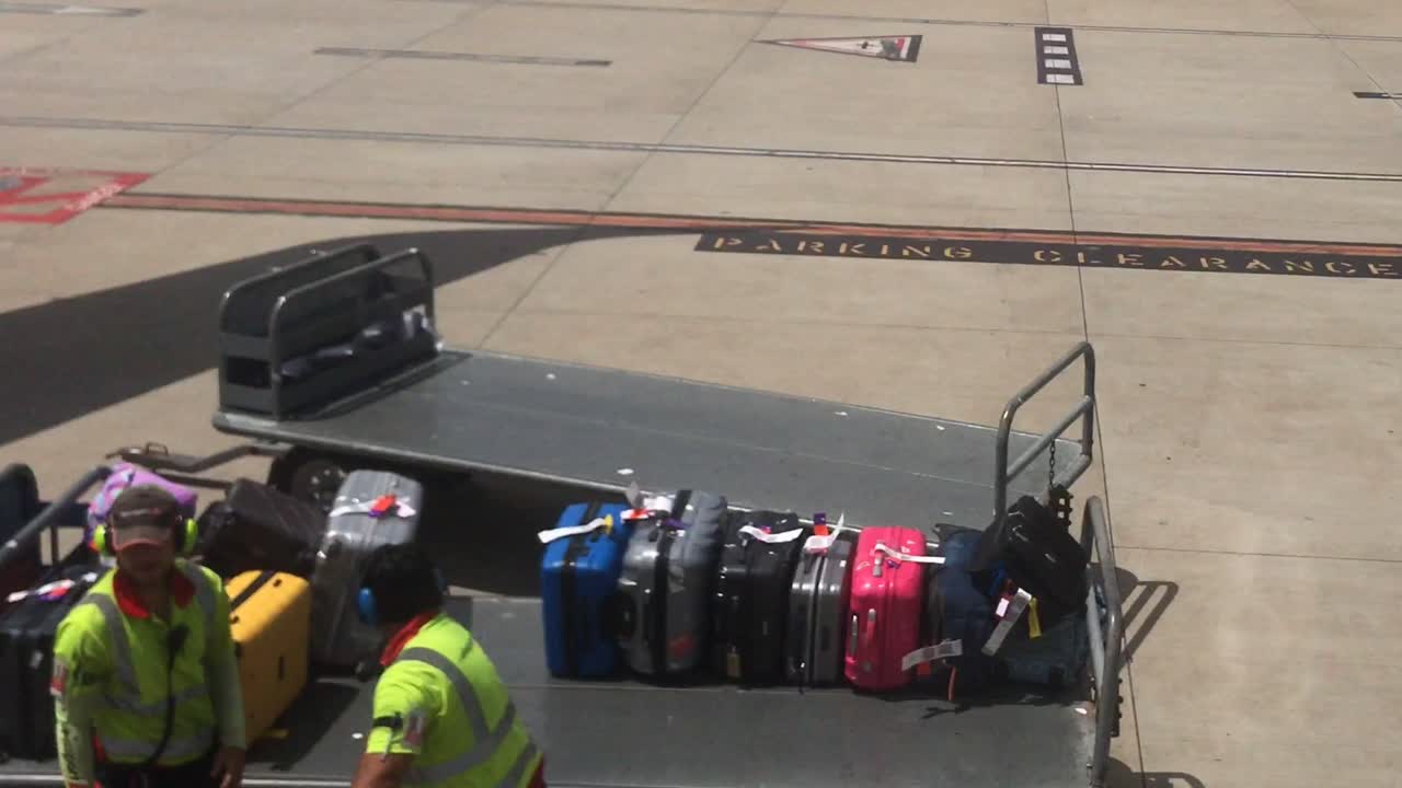 Two young male baggage handlers wearing high visibility vests unloading bags onto a luggage trolley on the tarmac at the airport
