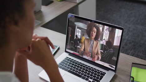 african american businesswoman sitting at desk using laptop having video call with female colleague