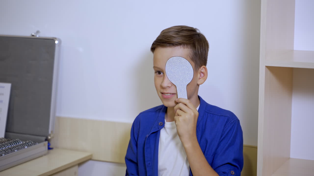 Test vision in eye clinic. Small boy is holding ophthalmology plate. Pediatric concept.