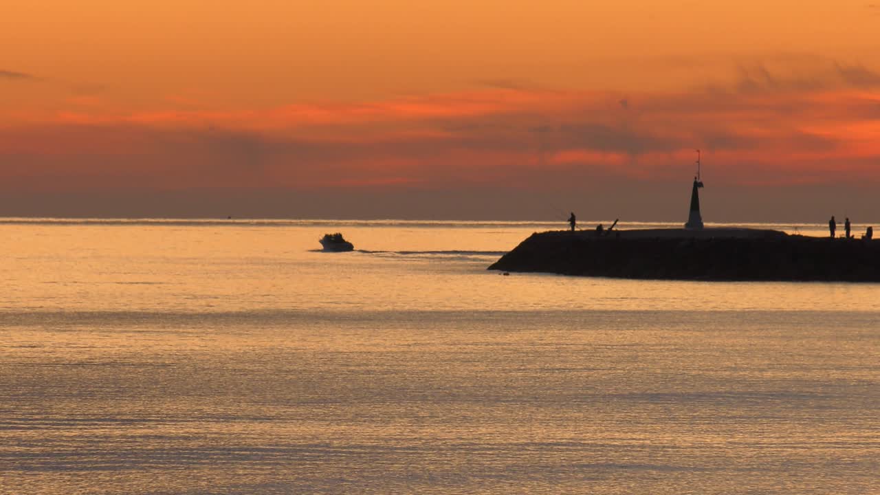 People fishing from harbor wall at dawn as motor boat heads out to sea