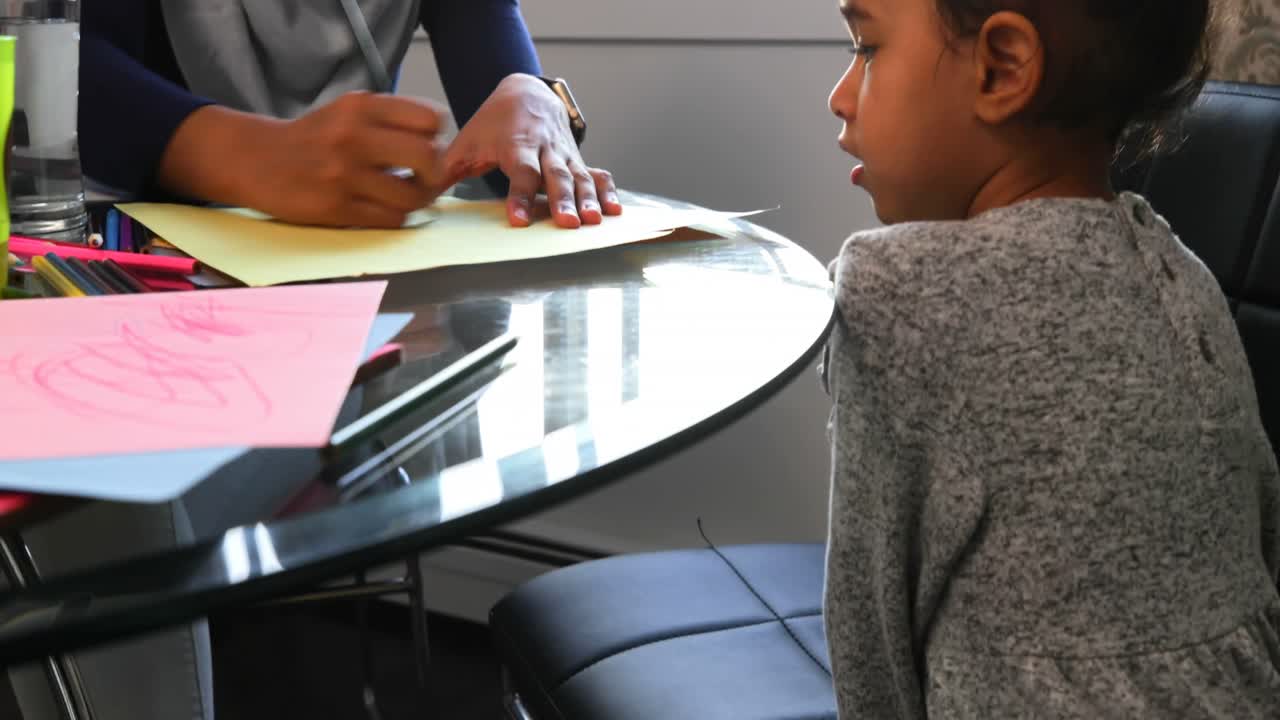 Giovane madre che aiuta la figlia con i compiti al tavolo 4K