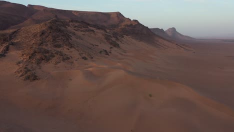 Drone-flying-over-desert-dunes-with-rocky-mountains-in-background,-Zagora-in-Morocco