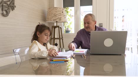 Girl painting next to her grandpa while working on a laptop at home