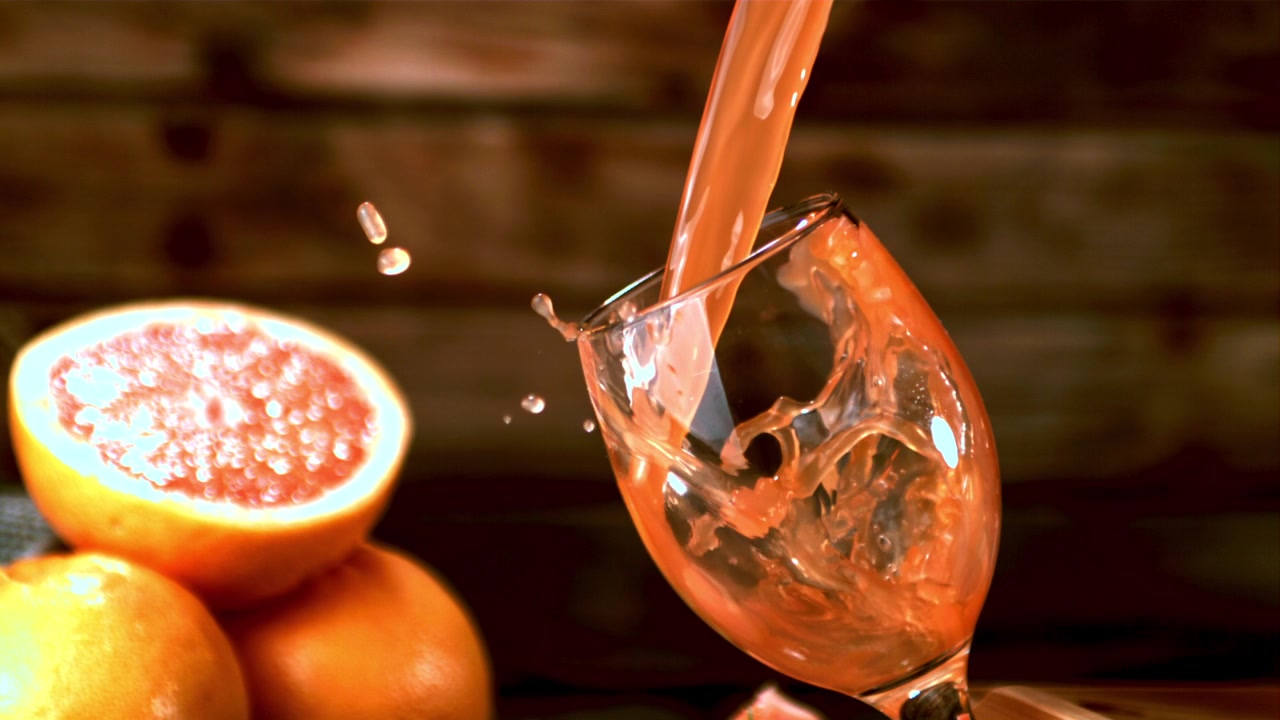 Succo di pompelmo che si versa in un bicchiere con schizzi al rallentatore.