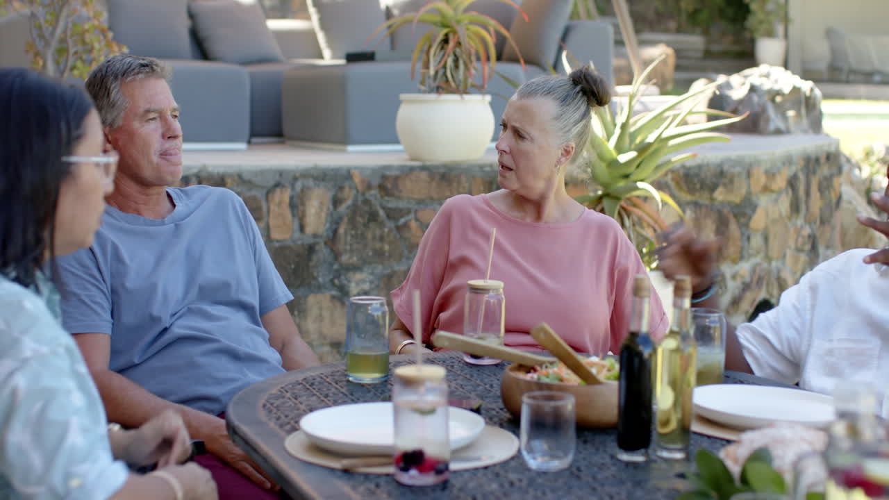 Senior diverse friends enjoying in garden lunch, sharing stories and laughter around table