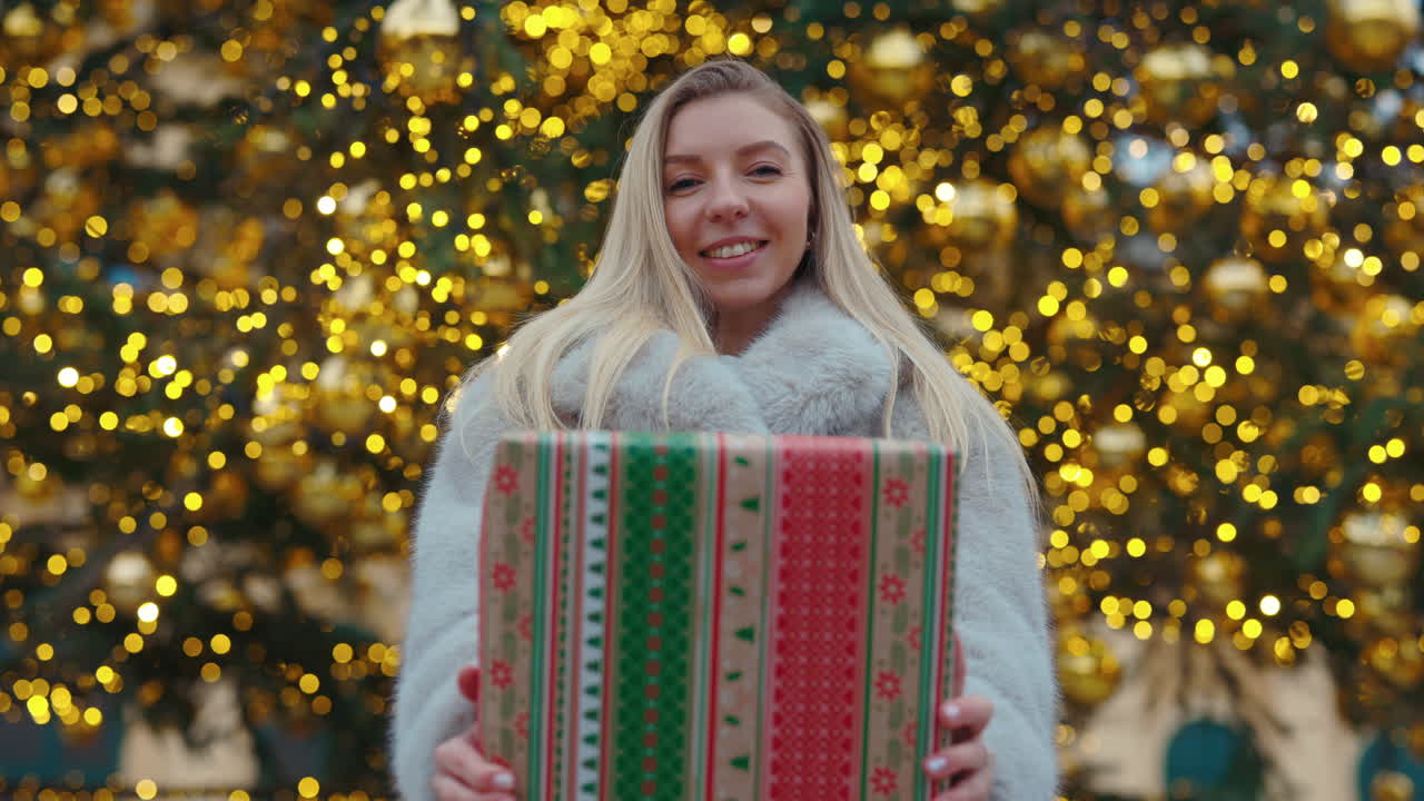 Woman Holding Christmas Gift in Front of Tree