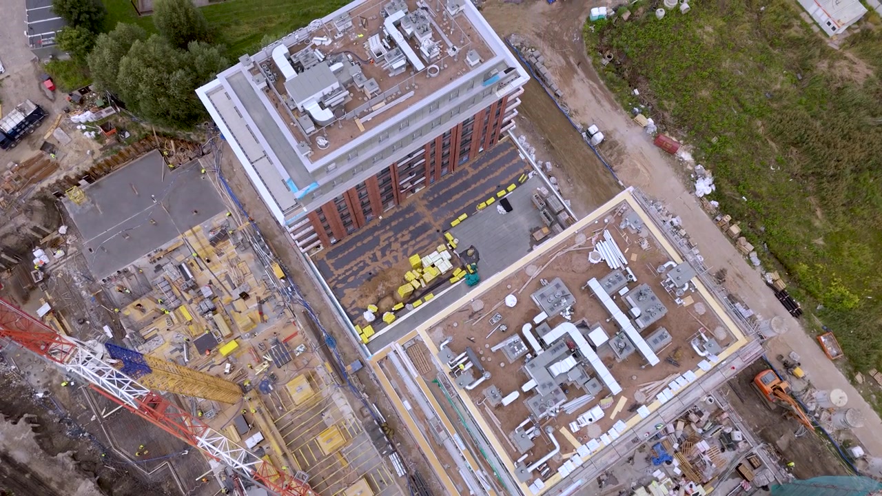 High-angle aerial drone view of an active construction site featuring a large tower crane, building structures, and equipment for real estate and urban development projects