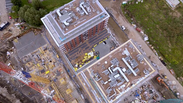 High-angle aerial drone view of an active construction site featuring a large tower crane, building structures, and equipment for real estate and urban development projects