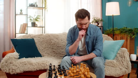young man playing chess alone making serious move deep thinking strategy concentration home sofa