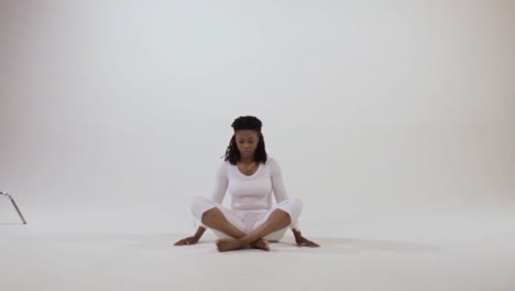 black woman with bowed head and crossed legs, looks forward then places her hands on her knees with fingers in a mudra for meditation