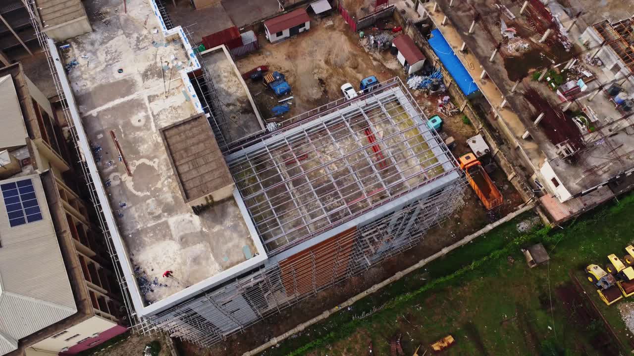 Aerial of a large building under construction in Abuja, Nigeria. A construction worker walks over the rooftop while the drone flies over and tilts down