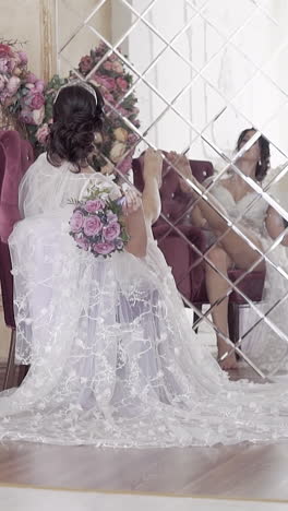 brunette bride with long lacy train and rose bouquet touches mirror with leg slow motion backside view