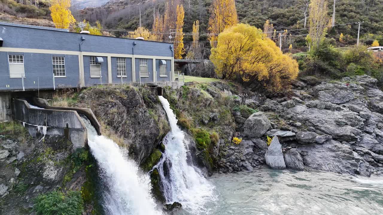 Drone captures hydroelectric plant and waterfall in Queenstown, New Zealand, with vibrant autumn foliage and dynamic water flow
