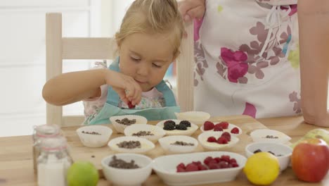 Little-girl-placing-berries-on-muffins