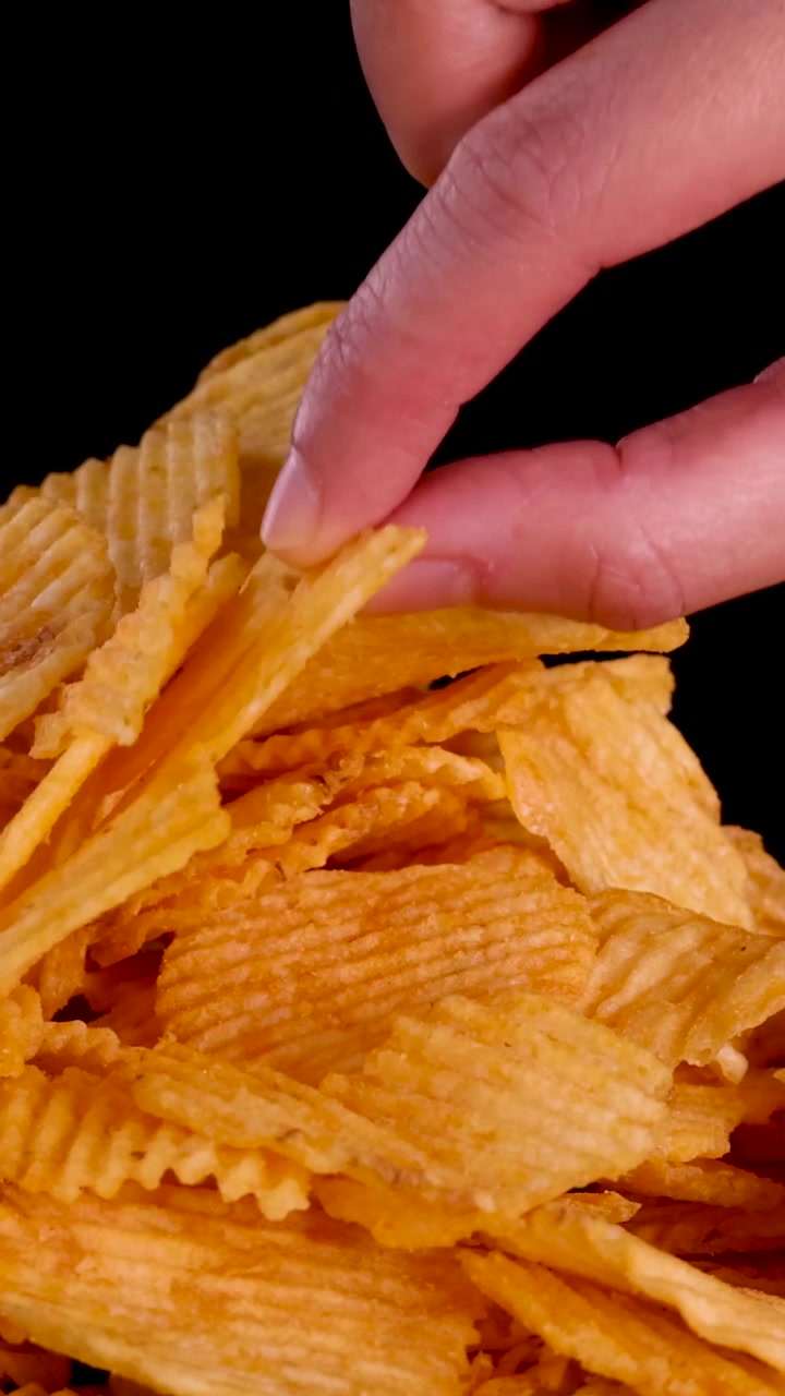 Una mano afferra un mucchio di patatine fritte dorate e ondulate su sfondo nero