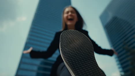 low angle view of a person's foot and laughing face, with buildings in the background