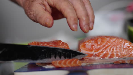 slicing fresh raw salmon fillet by hand with knife for sashimi preparation. close-up