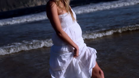 hermosa rubia caminando en vestido blanco en un día soleado en la playa