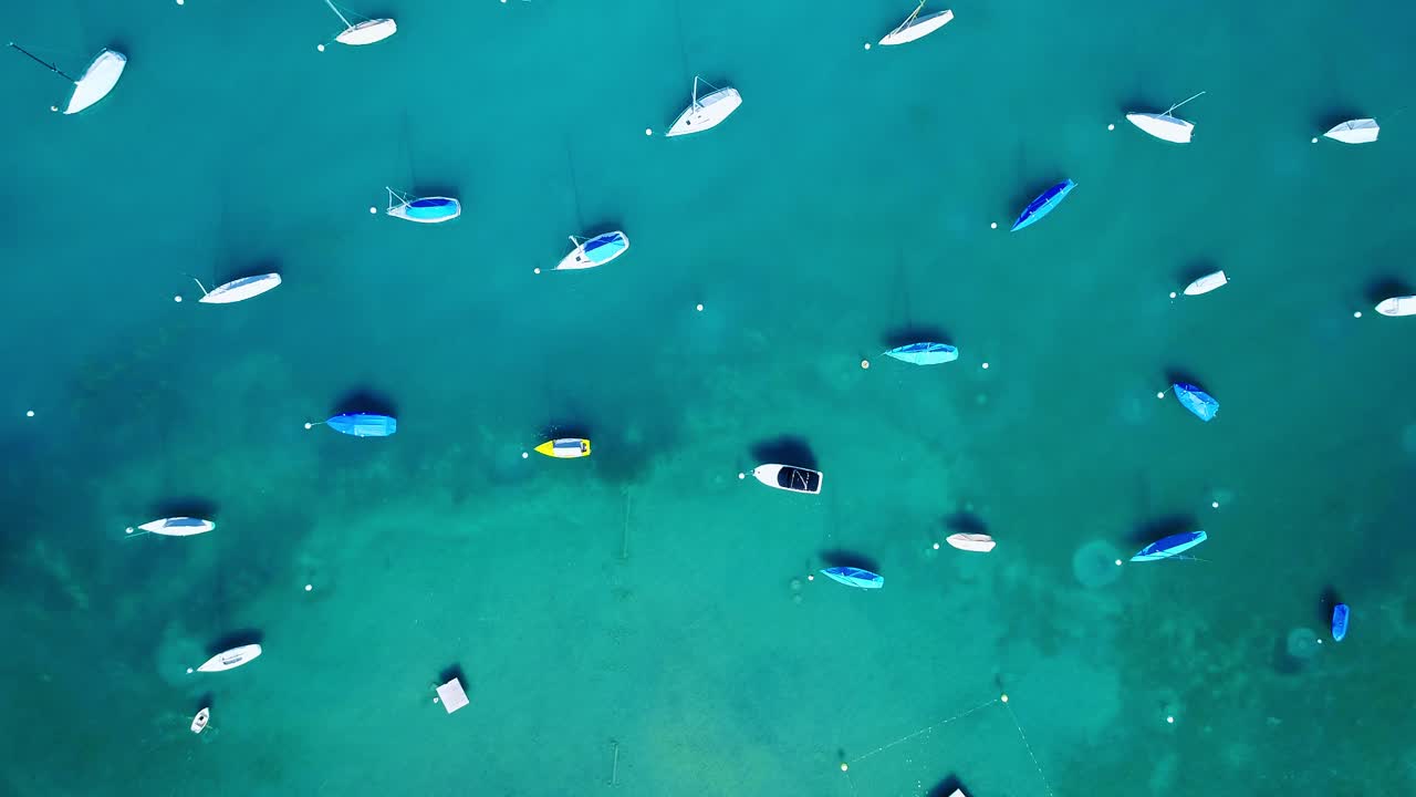 Boats scattered on clear blue water, vibrant top-down view, calm, idyllic vibes