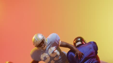 Video-Verschiedener-American-Football-Spieler,-Die-Mit-Dem-Ball-Auf-Gelbem-Bis-Orangefarbenem-Hintergrund-Angreifen