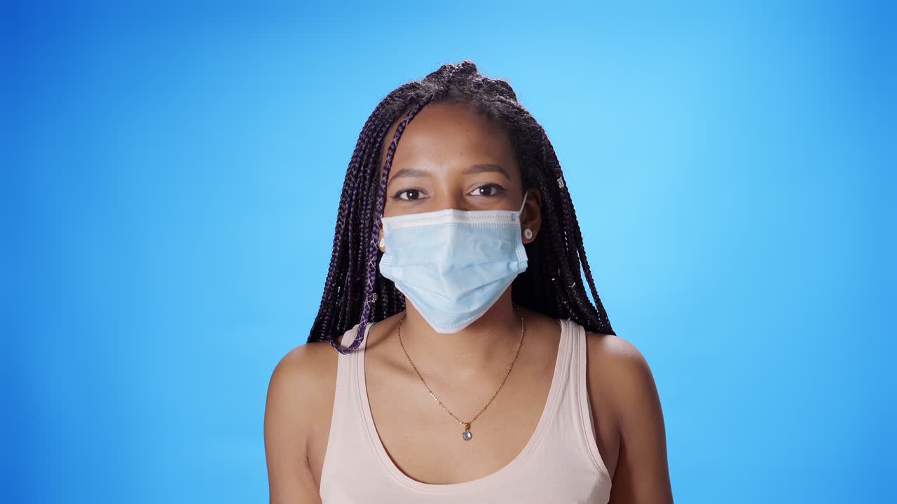 Portrait of a smiling black African American woman looking at the camera putting on and taking off a mask on a blue background. Chroma key background.