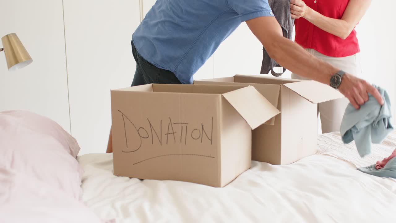 Senior couple sorting clothing into three boxes labeled DONATION on bed after deciding to donate