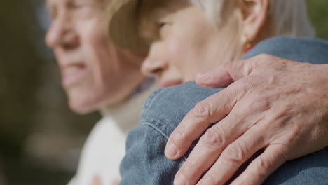 Close-Up-Of-An-Elderly-Husband-Embracing-His-Wife-And-Talking-With-Her-While-Spending-Time-In-Park-On-Sunny-Autumn-Day