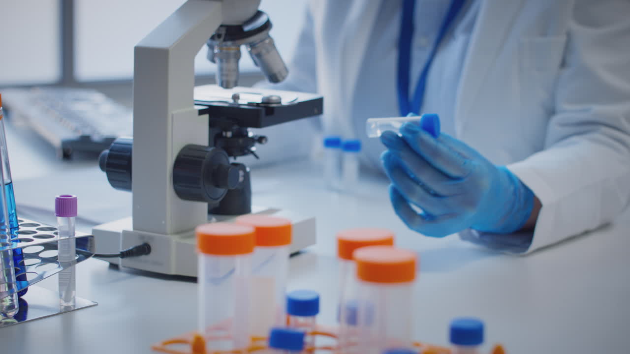 primer plano de un trabajador de laboratorio que lleva a cabo investigaciones utilizando un microscopio con un tubo de ensayo etiquetado upsilon