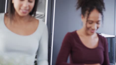 Happy-biracial-lesbian-couple-preparing-food-and-talking-in-kitchen,-in-slow-motion