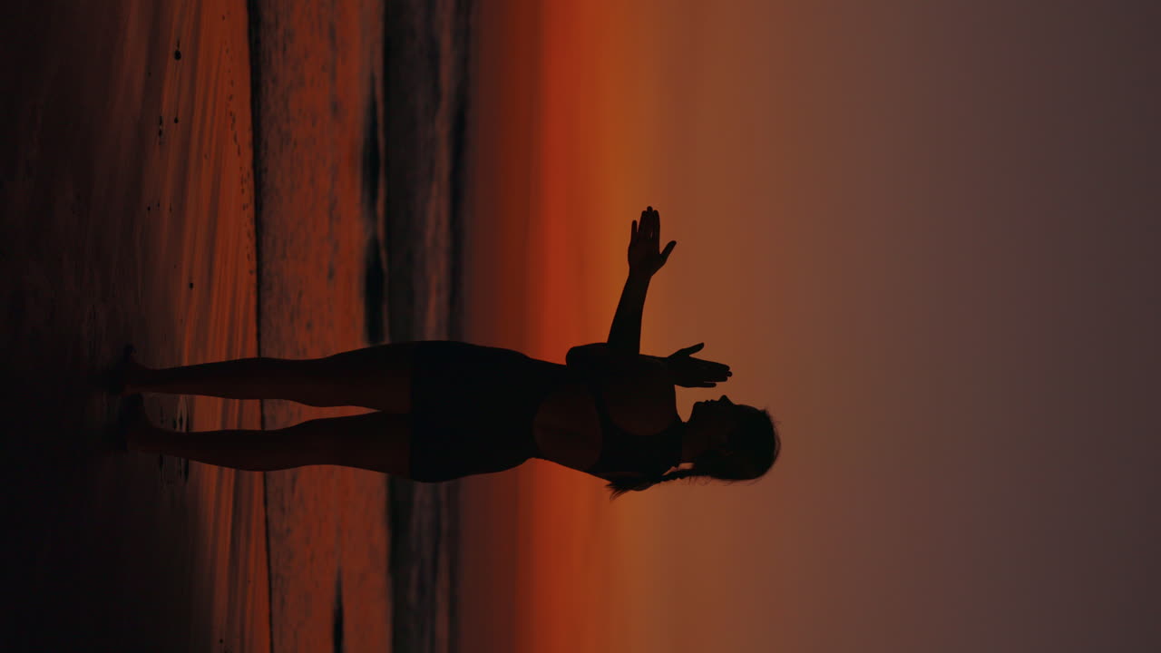 Silhouette of woman doing yoga on the beach at sunset