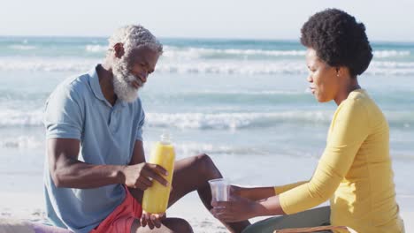 Happy-african-american-couple-having-picnic-on-sunny-beach