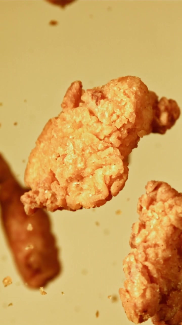 Pezzi di pollo fritto croccanti e dorati che cadono al rallentatore.