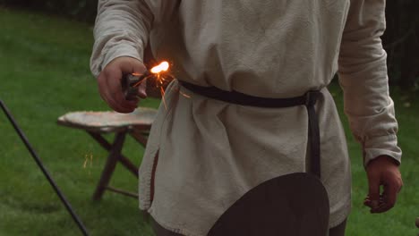 a revolutionary war reinacter blacksmith pulls a piece of metal out of hot coals with sparks coming off